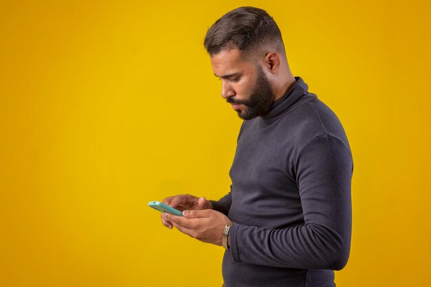 Un homme à barbe portant une chemise noire tenant un téléphone portable avec diverses expressions faciales