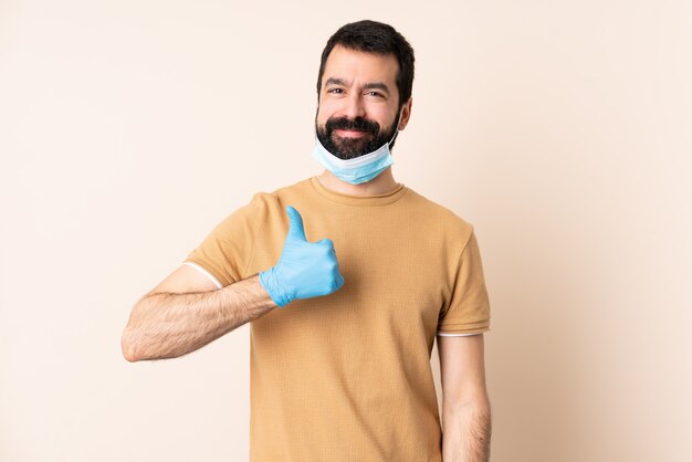 Homme à barbe protégeant contre le coronavirus avec un masque et des gants sur un mur isolé donnant un geste du pouce levé