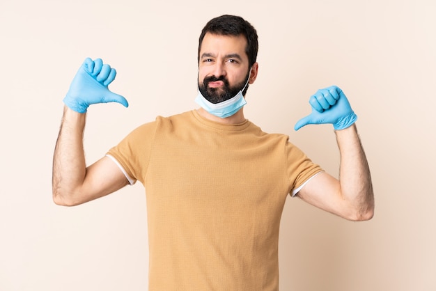 Homme à barbe protégeant du coronavirus avec un masque et des gants sur un mur isolé, fier et satisfait de lui-même