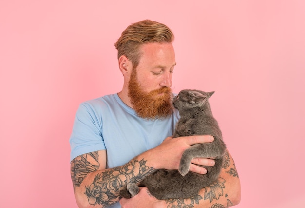 L'homme avec la barbe et les tatouages caresse un chat gris