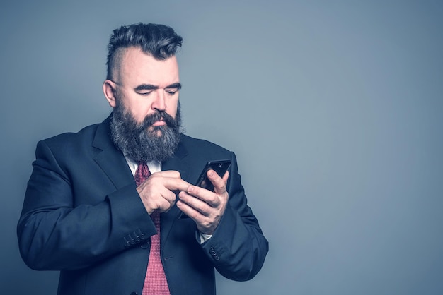 Homme barbu adulte en costume tenant un téléphone sur fond gris