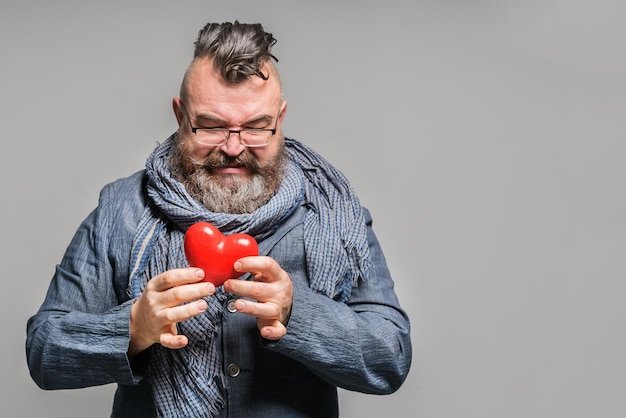 Photo homme barbu adulte dans une veste bleue et une écharpe tenant un coeur rouge