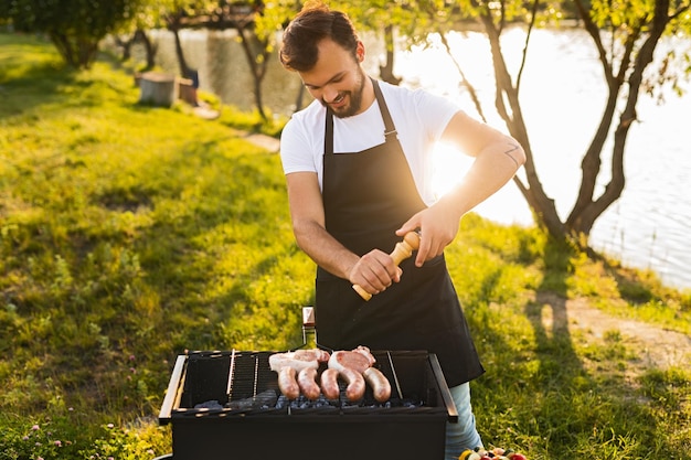 Photo homme barbu ajoutant des épices à la viande sur le gril