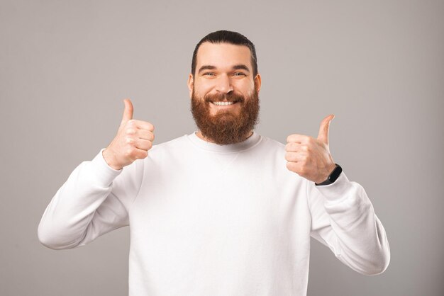 Un homme barbu amical montre deux pouces vers le haut tout en souriant à la caméra