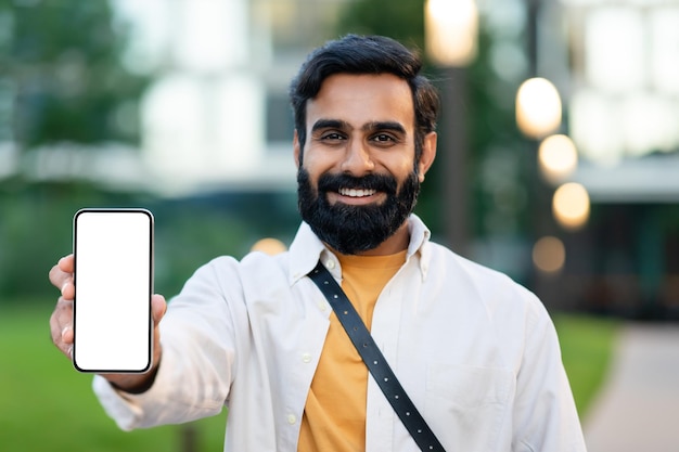 Un homme barbu arabe montrant un écran vide de téléphone dans une zone urbaine