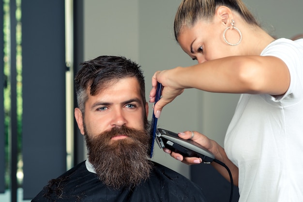 Homme barbu assis dans un fauteuil dans un salon de coiffure pendant que le coiffeur se rase la barbe avec un rasoir dangereux. Coiffage et coupe de la barbe.