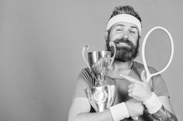 Homme barbu Athlète couronné de succès Première place Réalisation sportive Champion de tennis Gagner un match de tennis Célébrer la victoire Un homme athlétique tient une raquette de tennis et un gobelet d'or Un joueur de tennis remporte le championnat