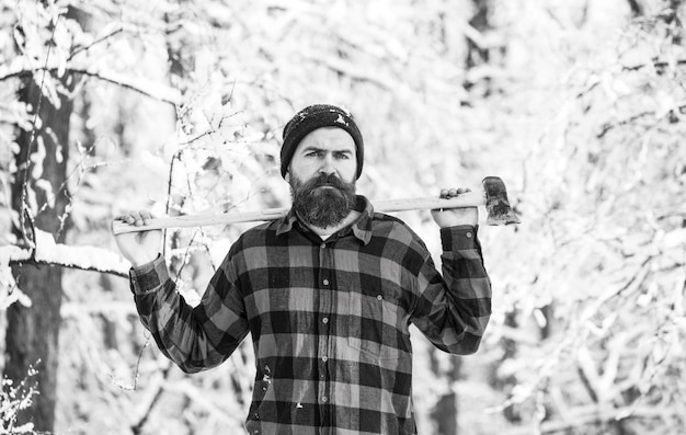 Homme barbu attrayant à l'extérieur en hiver. Un homme dans une forêt d'hiver. Un bûcheron travaillant dans la forêt. Homme inspectant des arbres en bois. Homme dans un paysage d'hiver. Homme du jour du dimanche avec une hache dans la forêt.