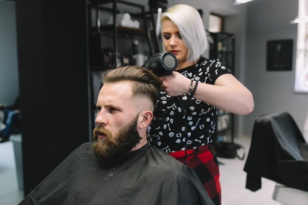 Homme barbu au salon de coiffure avec sèche-cheveux assis dans une chaise au salon de coiffure.