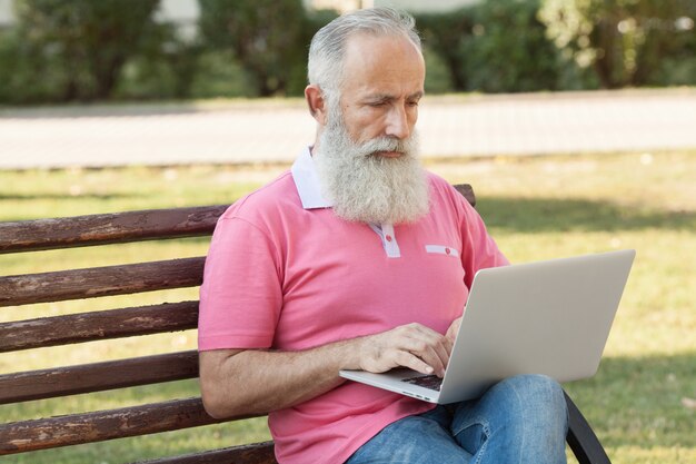 Homme barbu sur un banc à l'aide d'un ordinateur portable