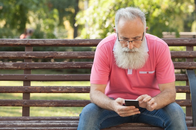 Homme barbu sur un banc à l'aide d'un téléphone