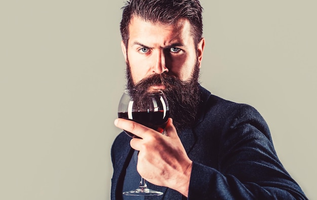 Homme barbu, barbu, sommelier dégustant du vin rouge. Sommelier, dégustateur avec verre de vin, cave, vigneron masculin. Homme tenant une coupe de champagne à la main.