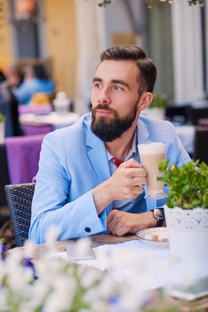 Un homme barbu boit du café dans un café.