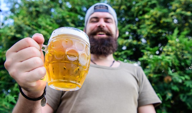 L'homme barbu brutal hipster tient une tasse de bière fraîche fraîche. L'homme se détend en appréciant la bière en été. Boisson alcoolisée et bar. La bière artisanale est jeune, urbaine et à la mode. Concept de santé. Culture de la bière distincte.