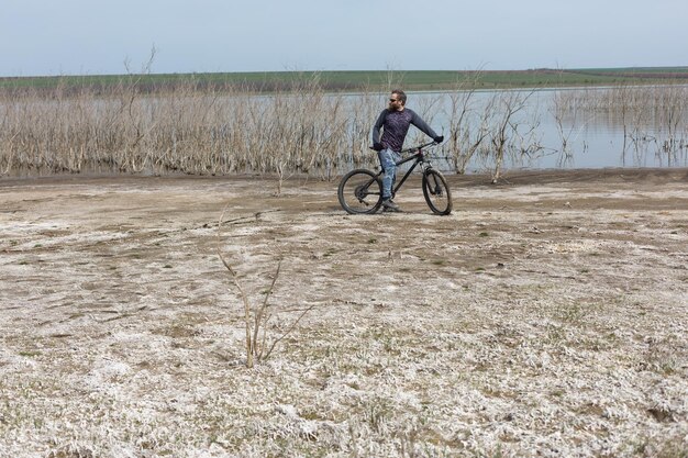 Un homme barbu brutal sur un vélo de montagne moderne Un cycliste dans un endroit désert de sel au bord du lac
