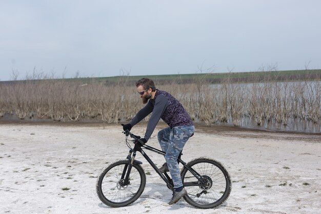 Un homme barbu brutal sur un vélo de montagne moderne Un cycliste dans un endroit désert de sel au bord du lac