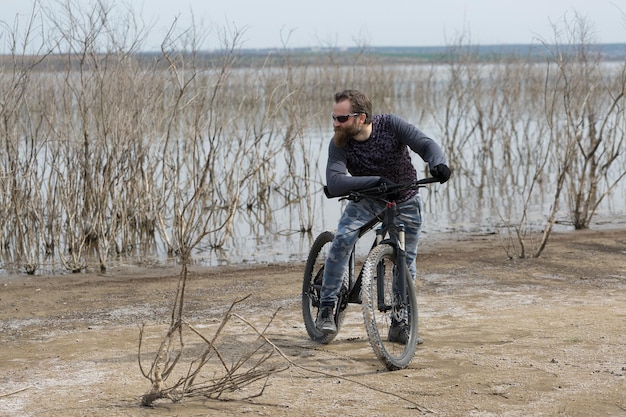 Un homme barbu brutal sur un vélo de montagne moderne Un cycliste dans un endroit désert de sel au bord du lac