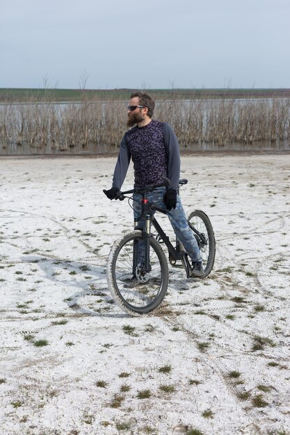 Un homme barbu brutal sur un vélo de montagne moderne Un cycliste dans un endroit désert de sel au bord du lac