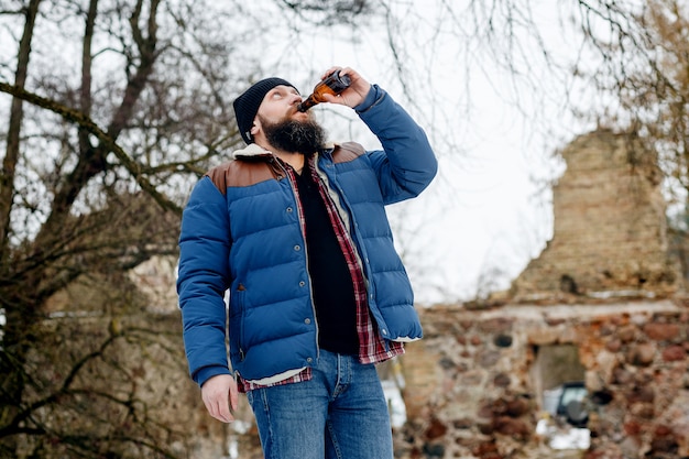 Homme barbu buvant de la bière en hiver dans le parc