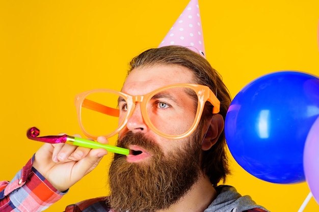 Homme barbu en casquette d'anniversaire avec corne de fête mâle en chapeau conique en papier et gros verres avec bruiteur