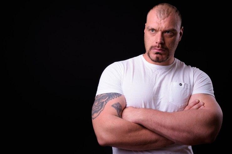Photo homme barbu chauve musclé à la macho contre le mur noir