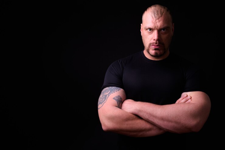 Photo homme barbu chauve musclé à la macho contre le mur noir