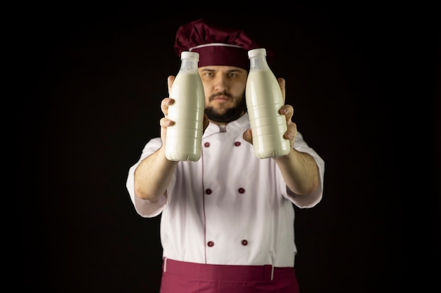 Photo homme barbu chef en uniforme détient deux bouteilles de lait, l'accent sur le lait