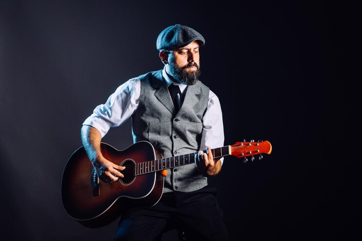 Photo un homme barbu en costume et chapeau assis et jouant de la guitare acoustique. portrait en studio