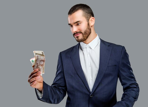 Homme barbu en costume détenant de l'argent comptant isolé sur fond gris.