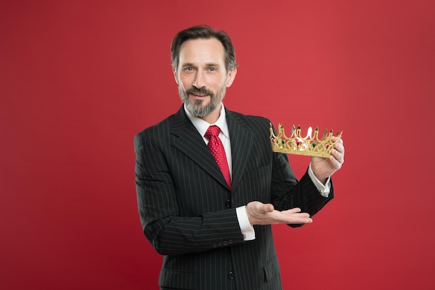 L'homme barbu en costume tient le symbole de la couronne d'or de la monarchie. Devenir roi cérémonie. Récompense et réalisation. Sentiment de supériorité. Être un humain supérieur. Attribut de monarchie. Traditions familiales de la monarchie.