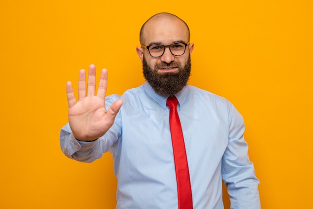 Homme Barbu En Cravate Rouge Et Chemise Portant Des Lunettes Regardant La Caméra Montrant Le Numéro Cinq Avec Palm Debout Sur Fond Orange