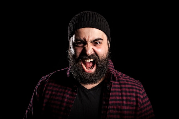 Homme barbu criant de colère sur fond noir en photo studio
