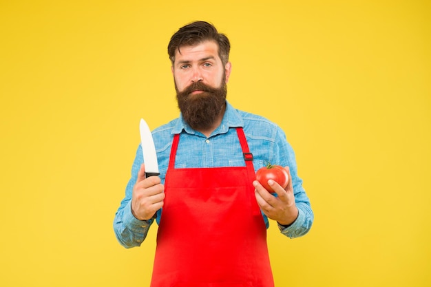 Homme barbu cuisiner des tomates rouges fraîches à l'aide d'un couteau tranchant cuisine de fond jaune