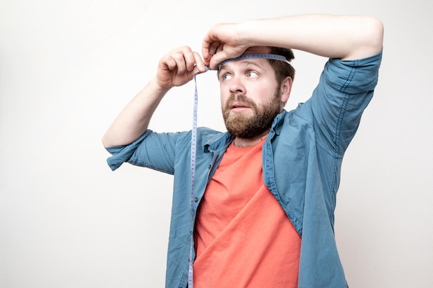 Un homme barbu curieux mesure le diamètre de sa tête avec un regard sérieux
