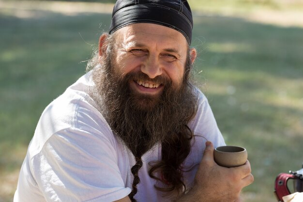 Un homme barbu dans un bandana boit du thé sur fond de nature.