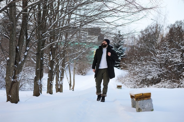 Homme barbu dans les bois d'hiver. Séduisante jeune homme heureux avec barbe marche dans le parc.