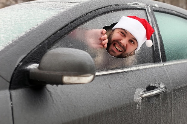 Homme barbu dans un bonnet rouge du Père Noël dans une voiture avec du verre brisé