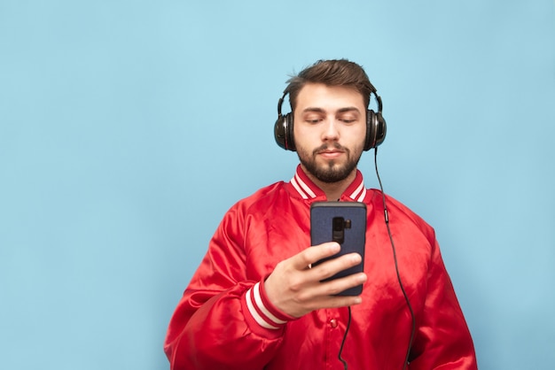 Homme barbu dans le casque debout sur un mur bleu avec un smartphone à la main