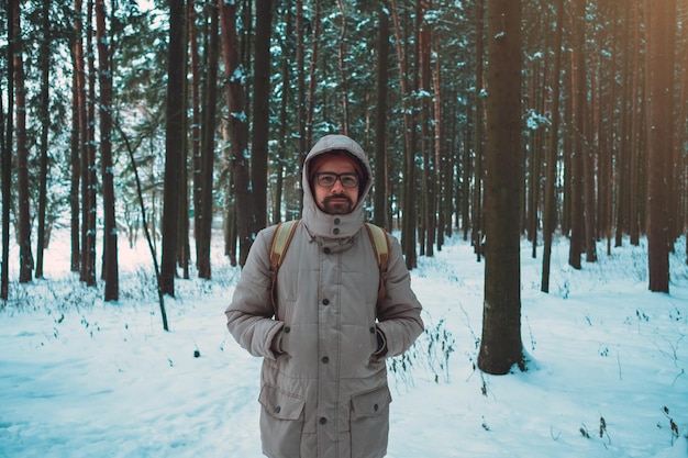 Un homme barbu dans un chapeau et un sac à dos se tient le dos en hiver dans une forêt de conifères sur la rivière Le concept de voyage d'hiver et de promenades dans les bois