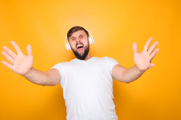 Homme barbu dans des écouteurs blancs chante fort et fait des gestes avec ses mains.