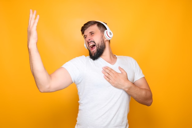 Homme barbu dans des écouteurs blancs chante fort et fait des gestes avec ses mains.