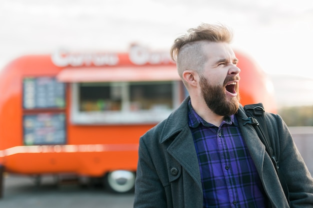 L'homme barbu dans la rue bâille avec la bouche ouverte se tient à un fond de camion de nourriture des gens endormis