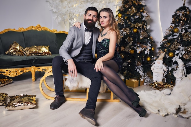 Homme barbu dans une veste grise et belle fille en robe verte brillante assis sur un traîneau d'hiver de Noël