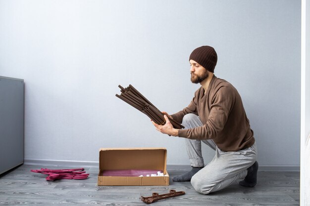 Un homme barbu déballe une boîte de pièces de mobilier.