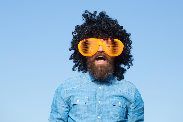 Homme barbu drôle fou avec perruque et lunettes amusantes sur fond de ciel Homme barbu drôle en perruque Bel homme barbu avec moustache en perruque