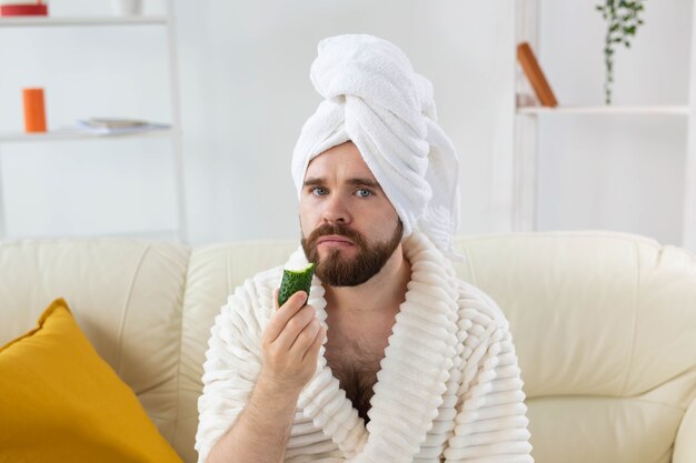 Homme barbu drôle tenant des tranches de concombre sur le visage spa à la maison corps et soins de la peau pour homme