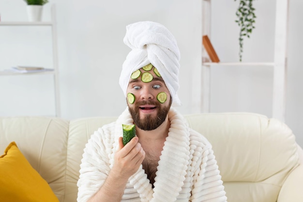 Homme barbu drôle tenant des tranches de concombre sur le visage spa à la maison corps et soins de la peau pour homme