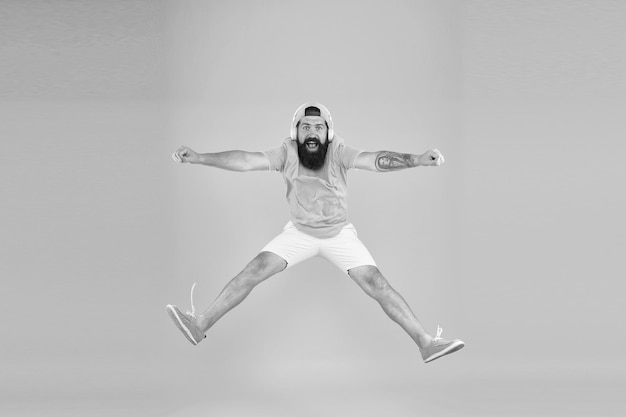 Homme barbu écouter de la musique mec heureux porter des écouteurs fête de vacances d'été hipster brutal sauter haut sa chanson préférée dj mature plein d'énergie sentir la liberté célébrer le succès