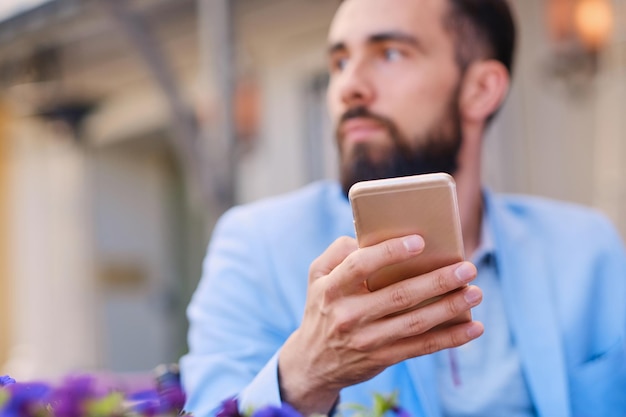 Homme barbu élégant dans une veste bleue à l'aide d'un smartphone.