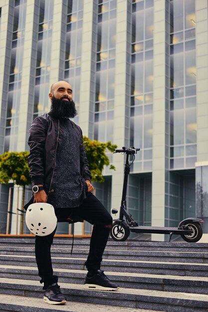 Homme barbu élégant sur une étape sur fond de scooter électrique.